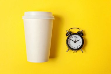 Sadece düz yatıyordu tasarım kağıt kahve Kupası ve sarı renkli şık arka planda çalar saat. Paket servisi olan restoran içki ve kahvaltı içecek. Günaydın uyanık kavramı uyandır. Üstten görünüm kopya alanı