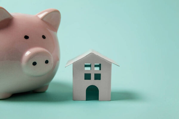 Just design with miniature toy house, piggy bank isolated on blue pastel colourful trendy background. Страхование ипотечного имущества мечта дом банковского инвестиционного кредита концепции. Копирование пространства
