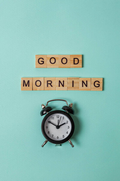 Simply flat lay design alarm clock and Inscription GOOD MORNING letters word on blue pastel colorful trendy background. Breakfast time. Good morning wake up awake concept. Top view copy space