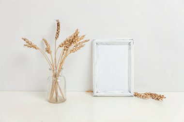 Dikey çerçeve mockup vahşi çavdar kokulu beyaz duvarının yakınında cam vazoda. Boş çerçeve tanıtım tasarım için sahte. Modern sanat için şablon çerçeveleme. Hygge İskandinav tarzı doğal Eko ev dekorasyonu