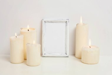 Dikey çerçeve mockup mum beyaz duvarının yakınında. Boş çerçeve tanıtım tasarım için sahte. Modern sanat için şablon çerçeveleme. Hygge İskandinav tarzı çalışma alanı. Doğal Eko ev dekorasyonu