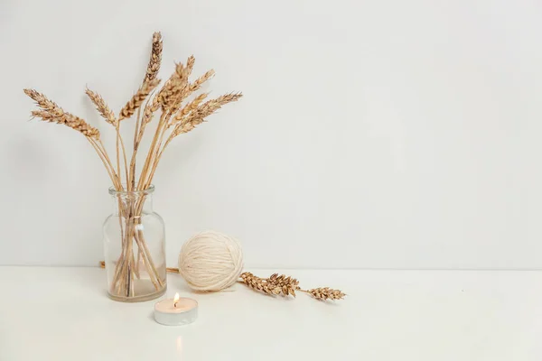 Natural eco home decor with wild rye bouquet in glass vase candle wool near white wall. Minimalism interior decoration lifestyle background. Hygge scandinavian style concept. Copy space place for text