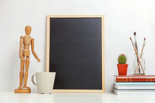 Home or office decor with mock up blank chalkboard on table near white wall. Minimalism interior workplace artist supplies decoration background. Hygge scandinavian style workspace concept