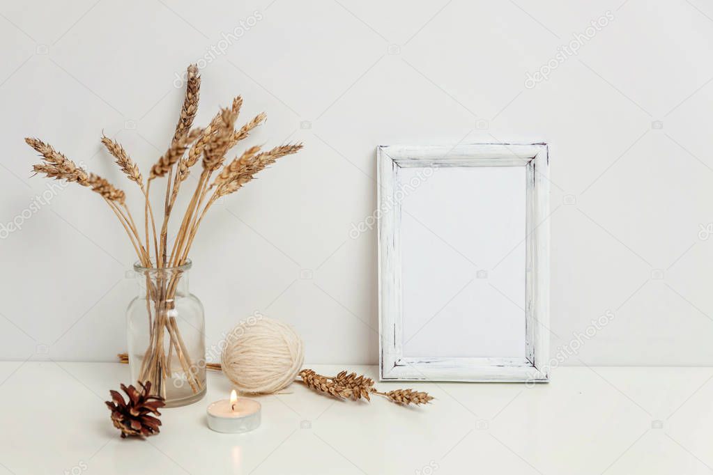 Vertical frame mockup with wild rye bouquet in glass vase near white wall. Empty frame mock up for presentation design. Template framing for modern art. Hygge scandinavian style Natural eco home decor