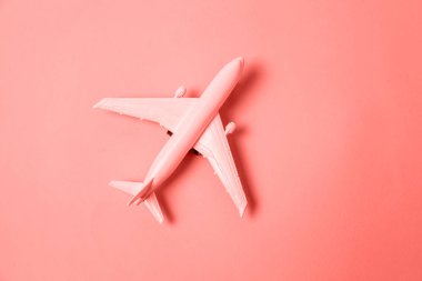Simply flat lay design miniature toy model plane colored in trendy color of year 2019 Living Coral background. Bright Macro color 16-1546. Travel by plane vacation adventure trip journey tour concept clipart