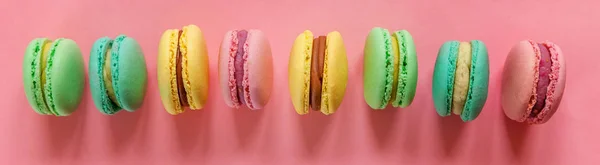 Sweet almond colorful pink blue yellow green macaron or macaroon dessert cake isolated on trendy pink pastel background. French sweet cookie. Minimal food bakery concept. Flat lay copy space banner