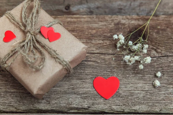 Gift box present wrapped craft paper with red hearts on rustic trendy old vintage wooden background.