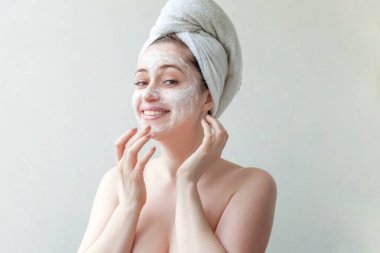 Bir havlu yüz izole beyaz arka plan üzerinde beyaz besleyici maske veya krem uygulayarak kafasına gülümseyen bir esmer kadın güzellik portresi. Cilt Bakımı temizlik spa kavramı relax