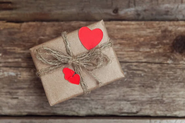 Hediye kutusu mevcut kaydırılan Kraft kağıt rustik trendy eski vintage ahşap zemin üzerine kırmızı kalp. 