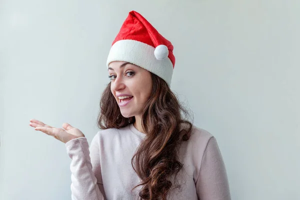 漂亮的女孩 留着红头发 戴着圣诞红帽 被白色背景隔离 看上去快乐而兴奋 年轻女人的肖像 真实的情感 圣诞佳节快乐 — 图库照片
