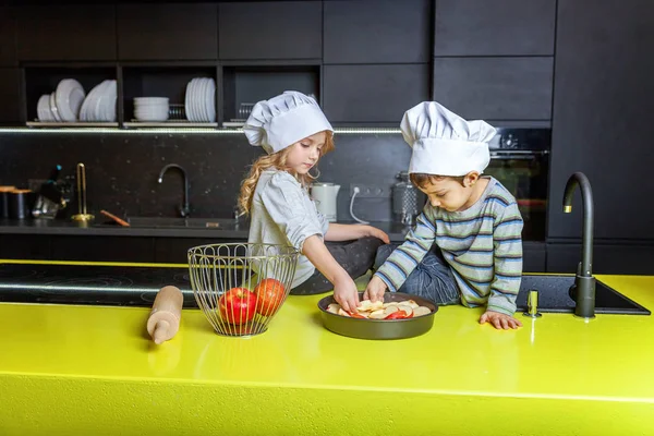 Kis gyerek lány és egy fiú a séf kalapját előkészítése sütni házi almás pite a konyhában — Stock Fotó