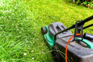 Bahçede çim biçme makinesiyle çim biçen bir adam. Bahçe işleri kırsal yaşam tarzı. Güneş ışığında taze yeşil çimlerin manzarası baharda ya da yaz mevsiminde bahçe manzarası