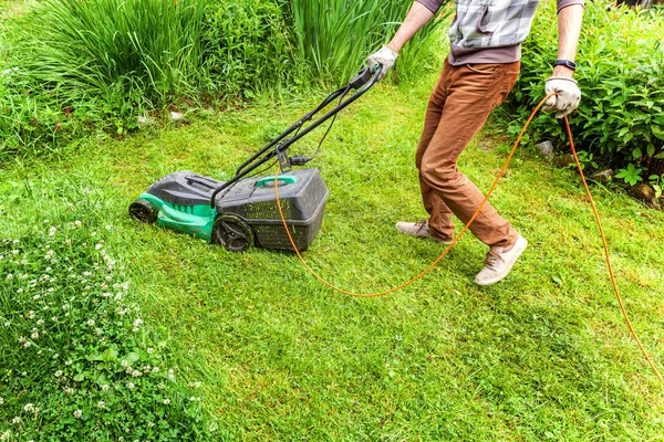Человек стрижет зеленую траву газонокосилкой на заднем дворе — стоковое фото