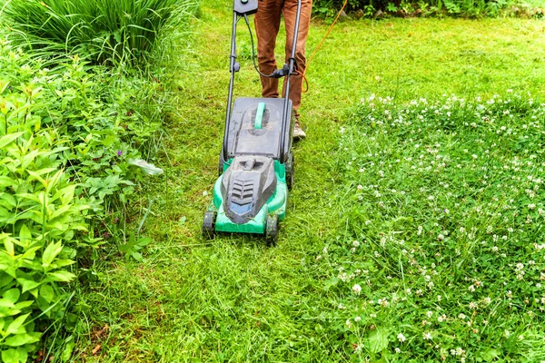 Man cutting green grass with lawn mower in backyard. Gardening country lifestyle background. Beautiful view on fresh green grass lawn in sunlight, garden landscape in spring or summer season