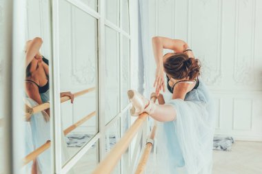 Genç Klasik Bale dansçısı kadın dans dersi. Güzel zarif balerin pratik bale pozisyonlar yakınındaki beyaz ışık salonda büyük ayna mavi tutu etekle