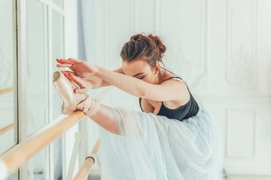 Genç Klasik Bale dansçısı kadın dans dersi. Güzel zarif balerin pratik bale pozisyonlar yakınındaki beyaz ışık salonda büyük ayna mavi tutu etekle