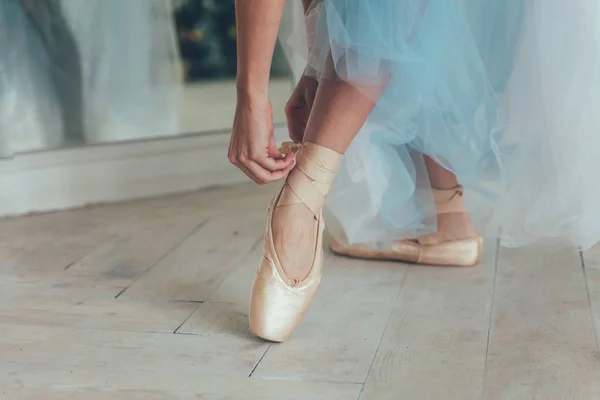 在白光大厅里 穿蓝色图图裙的芭蕾演员的手在腿上穿上尖鞋 舞蹈课中的年轻古典芭蕾舞演员 — 图库照片