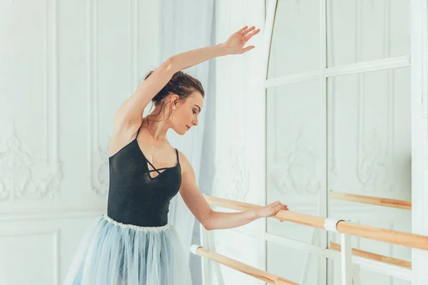 Young classical ballet dancer woman in dance class. Beautiful graceful ballerina practice ballet positions in blue tutu skirt near large mirror in white light hall