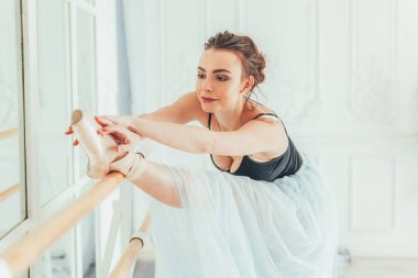 Genç Klasik Bale dansçısı kadın dans dersi. Güzel zarif balerin pratik bale pozisyonlar yakınındaki beyaz ışık salonda büyük ayna mavi tutu etekle