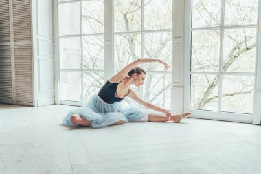 Genç Klasik Bale dansçısı kadın dans dersi. Mavi tutu etek beyaz ışık salonda büyük pencere yakınındaki güzel zarif balerin pratik bale pozisyonlar