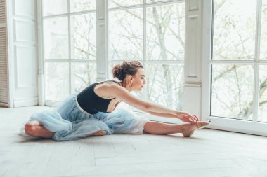 Genç Klasik Bale dansçısı kadın dans dersi. Mavi tutu etek beyaz ışık salonda büyük pencere yakınındaki güzel zarif balerin pratik bale pozisyonlar