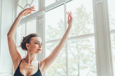 Genç Klasik Bale dansçısı kadın dans dersi. Mavi tutu etek beyaz ışık salonda büyük pencere yakınındaki güzel zarif balerin pratik bale pozisyonlar