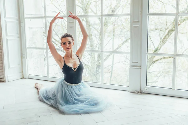 舞蹈课上年轻的古典芭蕾舞演员 美丽优雅的芭蕾舞演员练习芭蕾位置在蓝色 Tutu 裙子附近大窗口在白色光大厅 — 图库照片