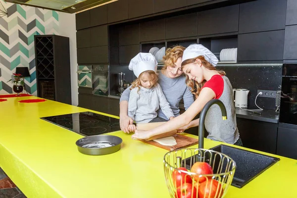 Happy family in kitchen. Mother and two children preparing dough, bake apple pie. Mom and daughters cooking healthy food at home and having fun. Household, teamwork helping, maternity concept