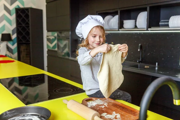 Little girl with chef hat, rolling pin preparing dough, bake homemade holiday apple pie in kitchen. Kid cooking healthy food at home and having fun. Childhood, household, teamwork helping concept
