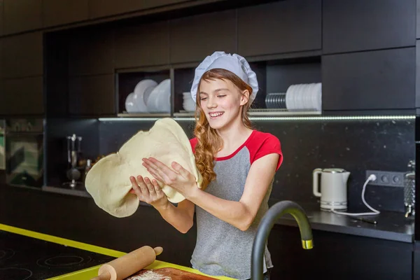 Teenage girl with chef hat, rolling pin preparing dough, bake homemade holiday apple pie in kitchen. Young woman cooking healthy food at home and having fun. Food, healthy eating, household concept