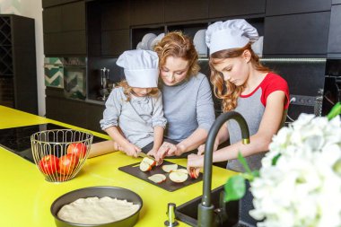 Mutlu aile mutfak. Anne ve iki çocuğu hamur, fırında elmalı turta hazırlanıyor. Anne ve kızı evde sağlıklı yemek pişirme ve eğleniyor. Yardım, ev içi, ekip çalışması annelik kavramı