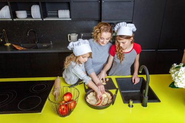 Mutlu aile mutfak. Anne ve iki çocuğu hamur, fırında elmalı turta hazırlanıyor. Anne ve kızı evde sağlıklı yemek pişirme ve eğleniyor. Yardım, ev içi, ekip çalışması annelik kavramı