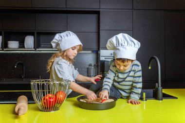 Küçük çocuklar kız ve oğlan şapka şef hazırlanması mutfakta ev yapımı elma pasta pişirin. Kız ve erkek kardeşim evde sağlıklı yemek pişirme ve eğleniyor. Çocukluk, ev içi, ekip çalışması yardımcı kavramı
