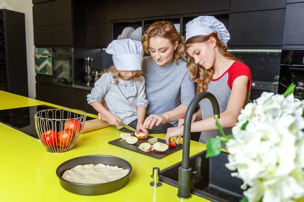 Happy family in kitchen. Mother and two children preparing dough, bake apple pie. Mom and daughters cooking healthy food at home and having fun. Household, teamwork helping, maternity concept