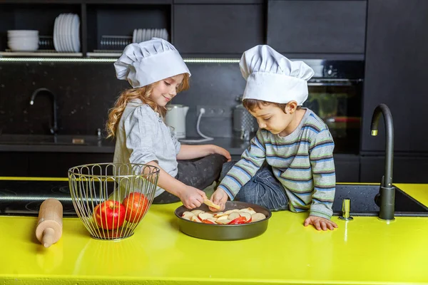 Küçük çocuklar kız ve oğlan şapka şef hazırlanması mutfakta ev yapımı elma pasta pişirin. Kız ve erkek kardeşim evde sağlıklı yemek pişirme ve eğleniyor. Çocukluk, ev içi, ekip çalışması yardımcı kavramı