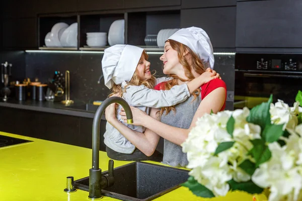 Two girls with chef hat hugging and having fun in kitchen. Sisters little kid and teenage girl cooking healthy food at home. Childhood, family, household, teamwork helping concept