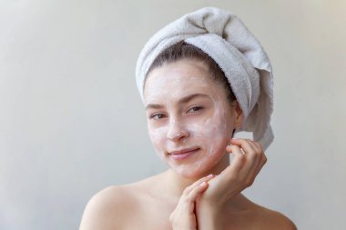 Bir havlu yüz izole beyaz arka plan üzerinde beyaz besleyici maske veya krem uygulayarak kafasına gülümseyen bir esmer kadın güzellik portresi. Cilt Bakımı temizlik spa kavramı relax