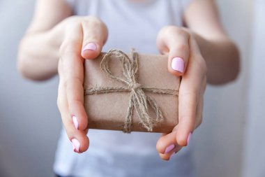 Küçük hediye kutusu sarılmış Kraft kağıt şerit ile tutan eller. Küçük Noel ve yeni yıl hediye kadın elinde dekore edilmiştir. Christmas Doğum günü Sevgililer günü kutlama hediyesi romantik kavramı