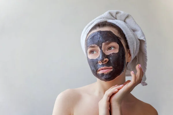 Bir havlu yüz beyaz arka planda siyah besleyici maske uygulayarak kafasına gülümseyen bir esmer kadın portresi güzellik izole. Cilt Bakımı temizlik spa rahatla kozmetik kavramı