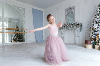 Dans sınıfındaki genç klasik balerin kız. Güzel, zarif balerin, bale pozisyonu pembe etekli, beyaz ışıklı salonda büyük aynanın yanında.