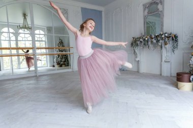 Dans sınıfındaki genç klasik balerin kız. Güzel, zarif balerin, bale pozisyonu pembe etekli, beyaz ışıklı salonda büyük aynanın yanında.