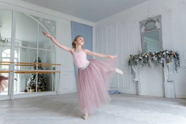 Young classical ballet dancer girl in dance class. Beautiful graceful ballerina practice ballet positions in pink tutu skirt near large mirror in white light hall