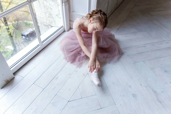 ダンスのクラスの若い古典的なバレエダンサーの女の子 美しい優雅なバレリーナでピンクチュチュスカート置く上のポイント靴近く大窓でホワイトライトホール — ストック写真