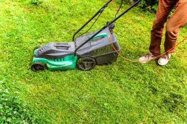 Bahçede çim biçme makinesiyle çim biçen bir adam. Bahçe işleri kırsal yaşam tarzı. Güneş ışığında taze yeşil çimlerin manzarası baharda ya da yaz mevsiminde bahçe manzarası