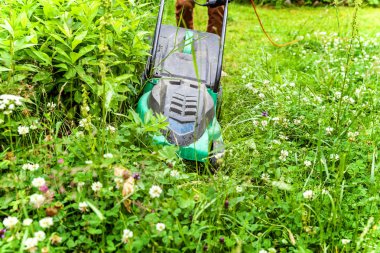 Bahçede çim biçme makinesiyle çim biçen bir adam. Bahçe işleri kırsal yaşam tarzı. Güneş ışığında taze yeşil çimlerin manzarası baharda ya da yaz mevsiminde bahçe manzarası