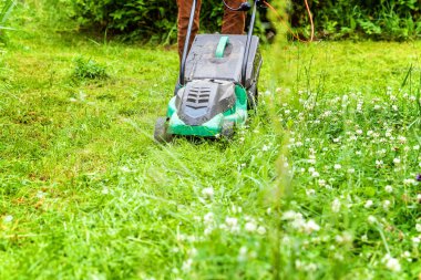 Bahçede çim biçme makinesiyle çim biçen bir adam. Bahçe işleri kırsal yaşam tarzı. Güneş ışığında taze yeşil çimlerin manzarası baharda ya da yaz mevsiminde bahçe manzarası
