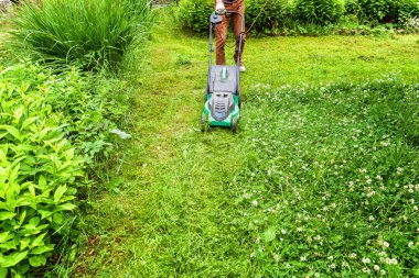 Bahçede çim biçme makinesiyle çim biçen bir adam. Bahçe işleri kırsal yaşam tarzı. Güneş ışığında taze yeşil çimlerin manzarası baharda ya da yaz mevsiminde bahçe manzarası