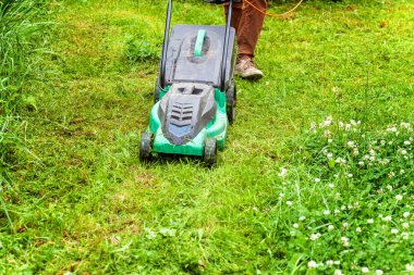 Bahçede çim biçme makinesiyle çim biçen bir adam. Bahçe işleri kırsal yaşam tarzı. Güneş ışığında taze yeşil çimlerin manzarası baharda ya da yaz mevsiminde bahçe manzarası