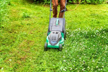 Bahçede çim biçme makinesiyle çim biçen bir adam. Bahçe işleri kırsal yaşam tarzı. Güneş ışığında taze yeşil çimlerin manzarası baharda ya da yaz mevsiminde bahçe manzarası