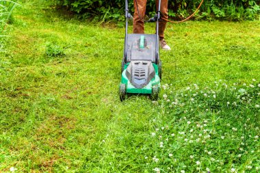 Bahçede çim biçme makinesiyle çim biçen bir adam. Bahçe işleri kırsal yaşam tarzı. Güneş ışığında taze yeşil çimlerin manzarası baharda ya da yaz mevsiminde bahçe manzarası